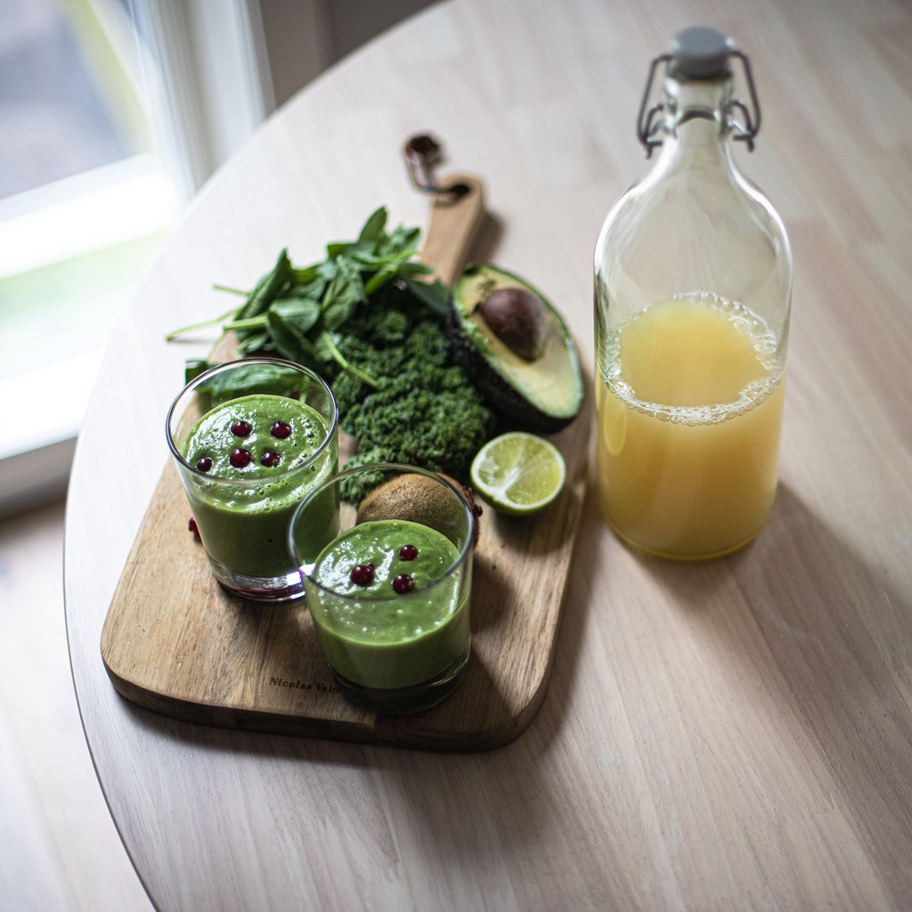 Grønn smoothie med spinat og grønnkål vist sammen med ingrediensene på et skjærebrett